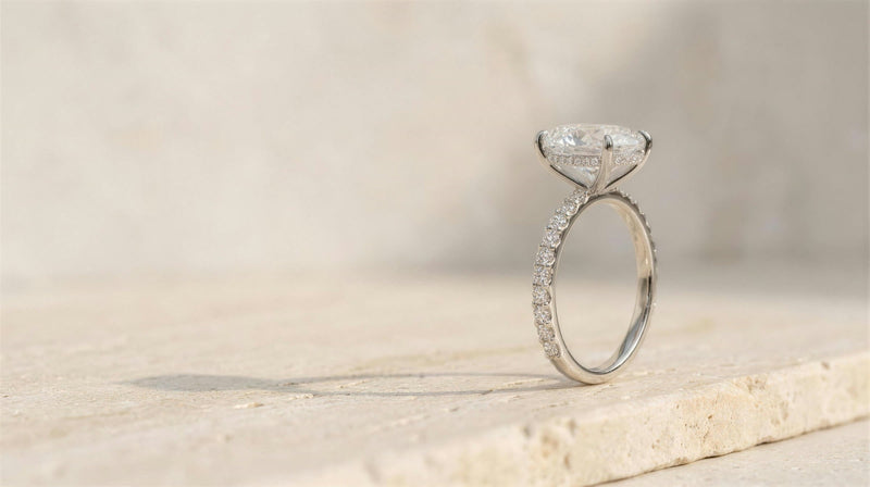 A 14K white gold oval pave engagement ring standing on a travertine ledge in soft daylight