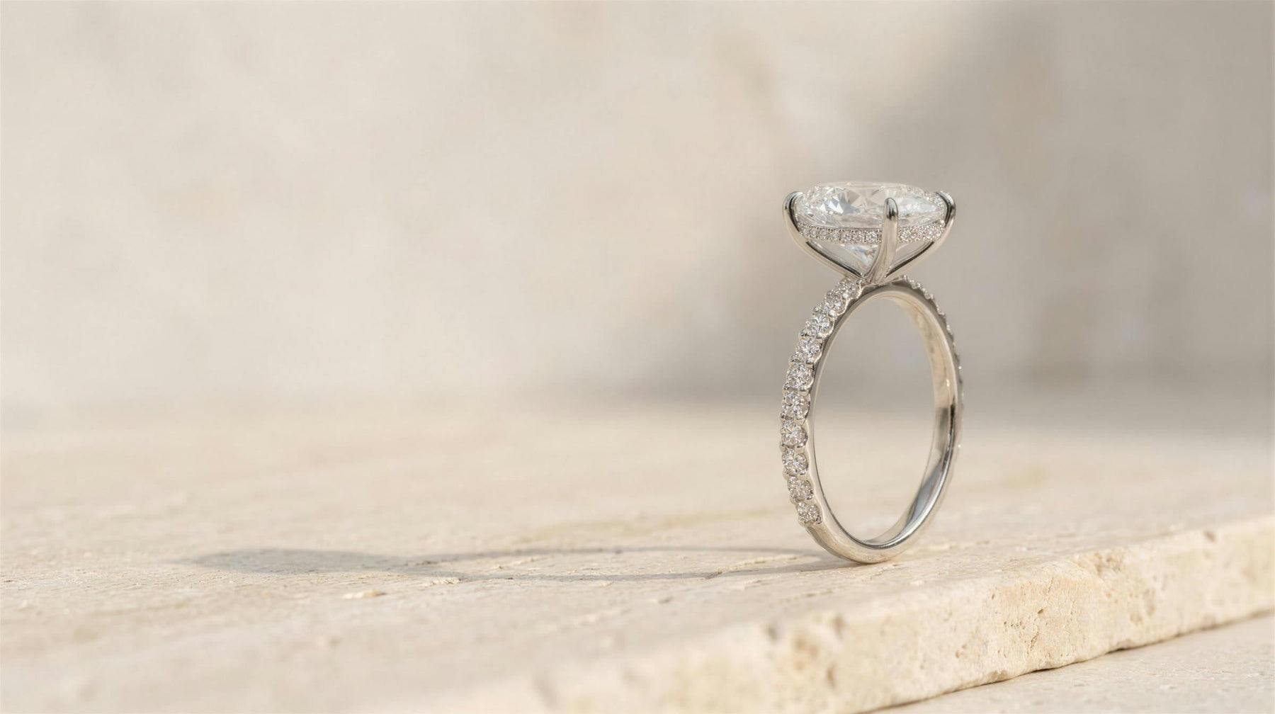 A 14K white gold oval pave engagement ring standing on a travertine ledge in soft daylight